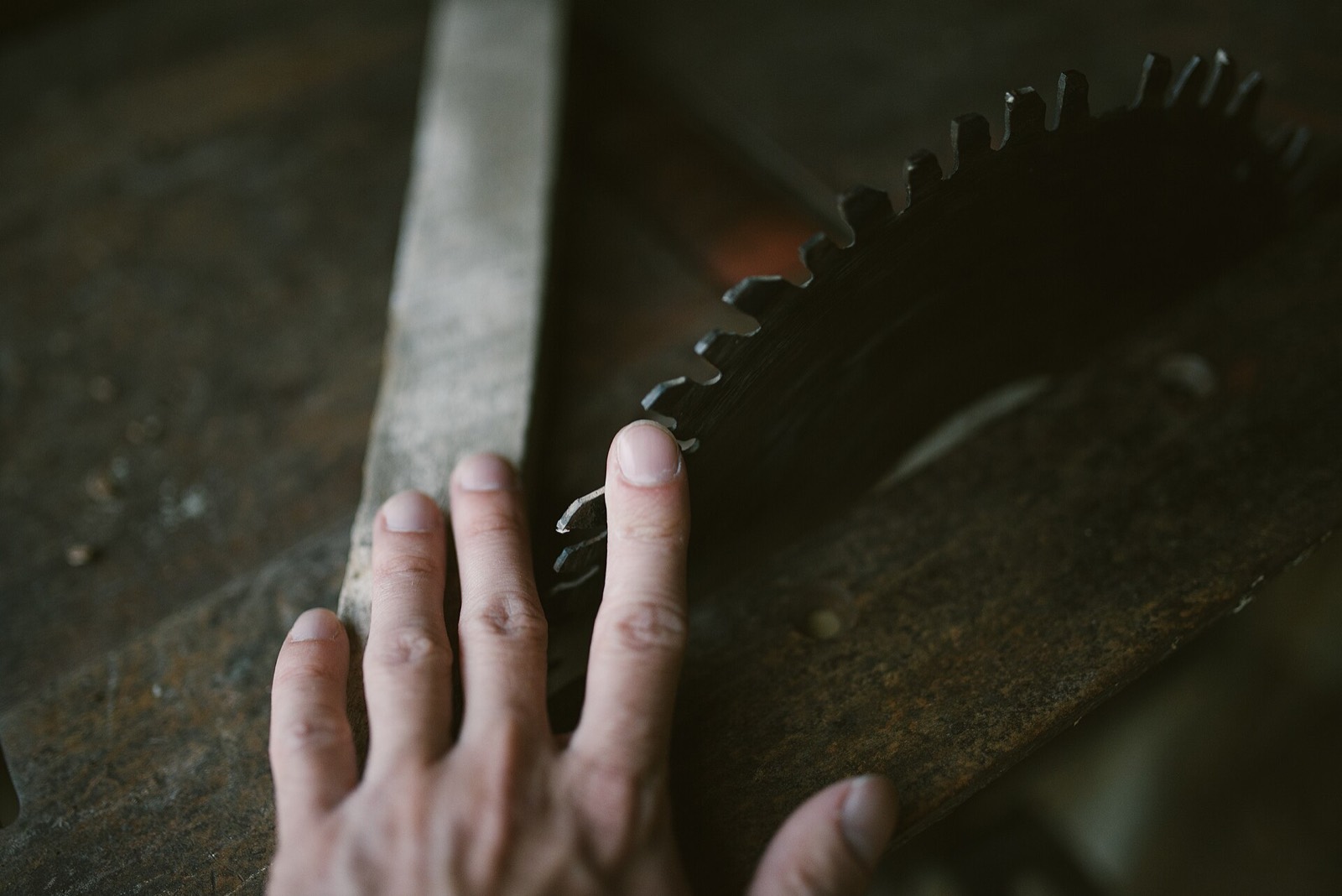 A hand resting on a saw blade at a wooden workbench